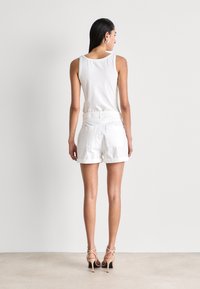 Hvit bomullstank topp parret med hvite shorts med skreddersydd passform, elastisk liv og to baklommer. Modellen har på seg nakne hæler.