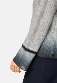 Grauer Gradient-Pullover mit weicher, flauschiger Textur. Hat schwarze Akzente an den Ärmeln und Seiten und zeigt einen Übergang von hell- zu dunkelgrau.