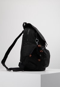 Mochila negra hecha de tela texturizada, con cierre de solapa, múltiples cremalleras y un pequeño llavero de juguete de mono adjunto a la cremallera.