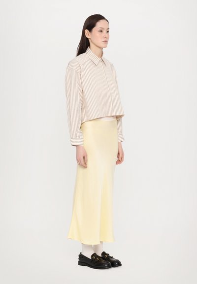 En kortermet stripet skjorte i beige og hvit, kombinert med et gult midiskjørt. Sorte loafers og hvite sokker fullfører antrekket. Enkelt design.