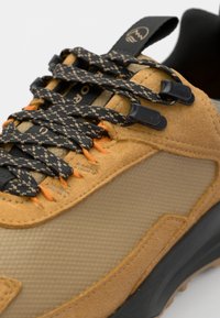 Brązowe skórzane i siateczkowe sneakersy z czarnymi i pomarańczowymi sznurowadłami, teksturowana cholewka i gumowa podeszwa. Posiadają aerodynamiczny kształt i kontrastowe akcenty.