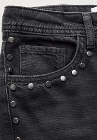 Jeans de mezclilla negra con un acabado texturizado, adornados con clavos plateados a lo largo del costado y un pequeño bolsillo delantero cerca de la cinturilla.