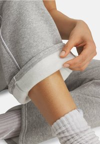 Grå sweatpants med en hvid fleecekanter, der viser en blød tekstur. Kanten er opfoldet for at afsløre det kontrasterende indre, mens en hånd justerer det.
