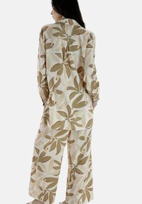 Completo floreale a due pezzi composto da una camicia a maniche lunghe con bottoni e pantaloni a gamba larga in tonalità beige, verde e rosso ruggine con grandi motivi a foglia.