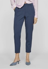 Pantalon bleu marine sur mesure à coupe ajustée, doté de poches latérales, d'une texture lisse et d'une taille mi-haute. Complété par des talons gris.