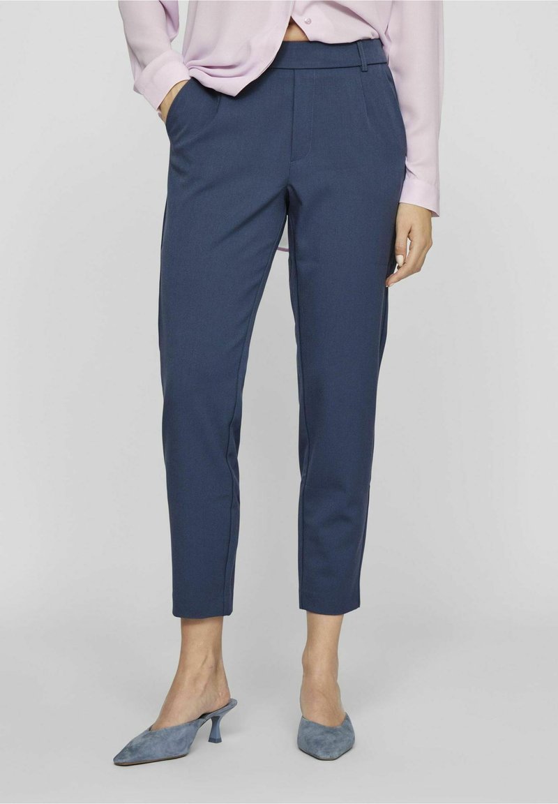 Pantalon bleu marine sur mesure à coupe ajustée, doté de poches latérales, d'une texture lisse et d'une taille mi-haute. Complété par des talons gris.