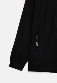 Veste noire avec une finition texturée, dotée d'une poche zippée et d'un poignet en velcro. Le design est minimaliste, sans motifs ni accents visibles.