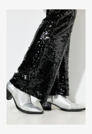 Czarne spódnice z cekinami z rozszerzanymi nogawkami i błyszczącą teksturą, w zestawie z metaliczno-srebrnymi botkami sięgającymi kostki, posiadającymi blokowy obcas i spiczasty czubek.