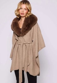 Poncho beige avec un large col en fausse fourrure marron, ceinture à nouer et côtés ouverts. Tissu doux et texturé, offrant une coupe ample et confortable.