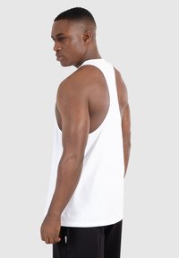 Weißes ärmelloses Tanktop mit weiten Armlöchern, aus weichem Baumwollmaterial. Der Rücken hat ein Racerback-Design und bietet einen lässigen Schnitt.
