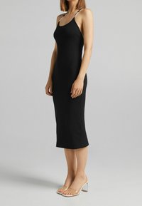 Abito midi nero a coste con spalline sottili e dettagli argentati. Abbinato a sandali con tacco trasparente. Tessuto liscio, design aderente.