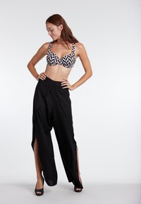 Black, flowing wide-leg pants with side slits, paired with a geometric patterned bikini top featuring triangular designs in black and white.