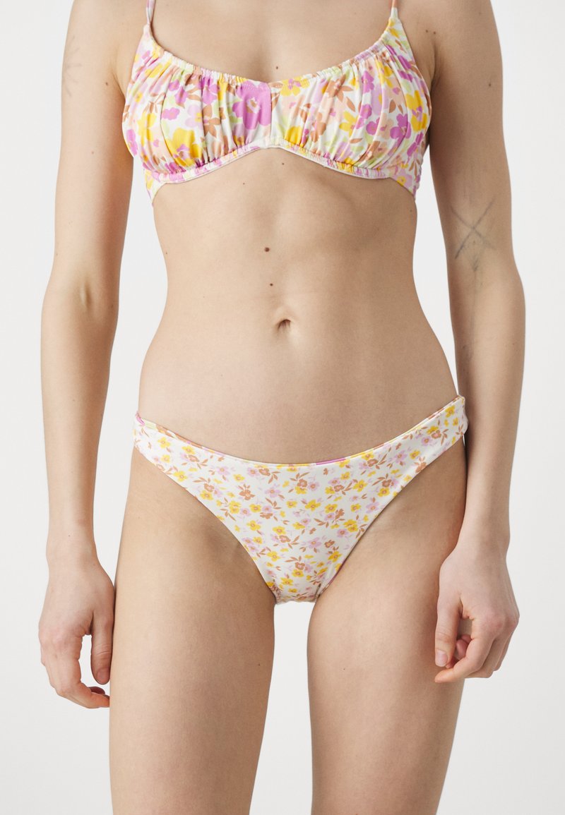 Ensemble de bikini floral comprenant un haut à volants dans des couleurs pastel avec des fleurs roses et jaunes, et un bas de bikini taille basse assorti. Texture de tissu lisse.