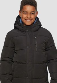 Veste à doudoune noire isolée avec capuche. Elle dispose d'une poche poitrine zippée et de boutons-pression. Texture lisse et design matelassé.