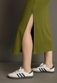 Olijfgroen, geribbeld midi-jurkje met een zijsplit, gecombineerd met wit-zwart Adidas Samba sneakers met een suède neuskap en veters.