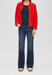 Rode cropped jas van een wolmix met een ritssluiting aan de voorkant, gecombineerd met donkerblauwe uitlopende spijkerbroeken en beige instapschoenen. Eenvoudig, functioneel ontwerp.