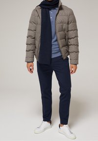 Chaqueta acolchada gris con costuras, bufanda azul marino, camisa polo azul y pantalones azul marino. Zapatillas blancas con detalles en azul marino. Texturas suaves y diseño estructurado.