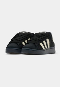 Melni zamšāda sporta apavi ar baltām svītrām un logotipu. Aprīkoti ar polsterētu apkakli, plakaniem aukliņām un zemu, gumijas zoli.