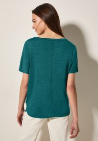 T-shirt teal à manches courtes avec un décolleté en scoop, présentant une couture au dos et une coupe décontractée, fabriqué en tissu doux et texturé.