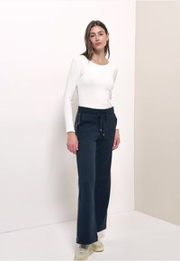 Pantalon bleu marine ample avec une taille à cordon de serrage, doté de bandes blanches sur les côtés, assorti à un haut blanc ajusté à manches longues.