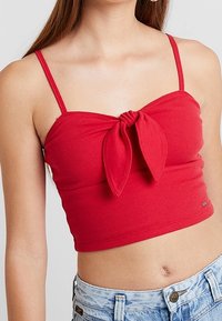 Röd ribbad croptop med en knutdetalj fram, tunna axelband och en tight design. Matchad med denimshorts.