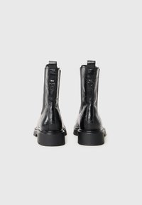 Bottines noires en cuir texturé avec une finition lisse, dotées d'une semelle en caoutchouc basse et d'accents métalliques décoratifs à l'arrière.