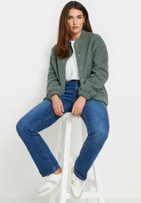 Green textured bomber jacket, white shirt, blue jeans, and white sneakers. The jacket features snap buttons and a relaxed fit.