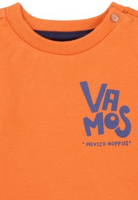 Pomarańczowa bawełniana koszulka z okrągłym dekoltem, z niebieskim napisem graficznym "VAMOS" oraz "MEXICO NOPPIES" nadrukowanym na przodzie.