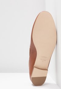 Bruine leren schoen met een lage hak, een gladde textuur en een lichtgekleurde zool. Kenmerken zijn "MADE IN ITALY" en maat 37.