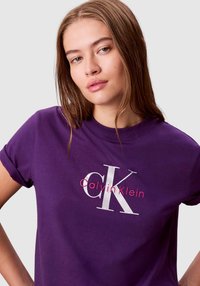 Fioletowy t-shirt z krótkim rękawem wykonany z bawełny, z białym i różowym logo Calvin Klein z przodu.