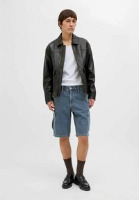 Giacca di pelle nera, canotta bianca a coste, pantaloni cargo in denim blu, calzini marroni e mocassini neri. Stile semplice, casual e funzionale.
