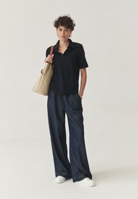 Polo a maniche corte blu navale, pantaloni in denim scuro larghi, sneakers bianche e una borsa a tracolla beige texturizzata.