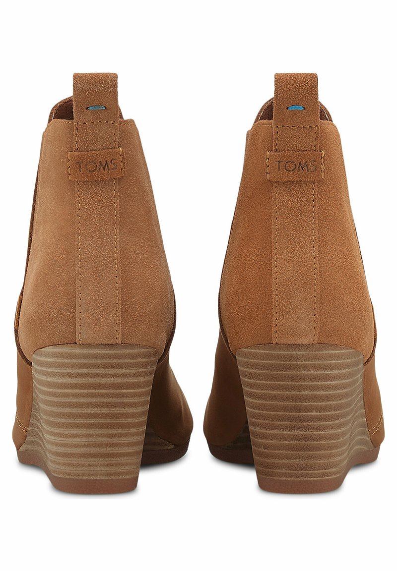 Botas de tobillo de ante marrón con tacón de cuña, que cuentan con un refuerzo en la parte del talón y una etiqueta de marca, lados texturizados y una suela estriada.