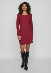 Vestido burdeos de manga larga con escote redondeado, hecho de tela suave, combinado con botas de cuero negro hasta la rodilla.