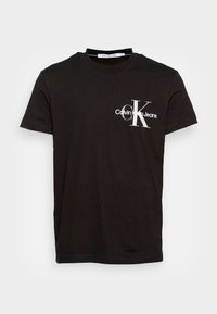 Černé bavlněné tričko s kulatým výstřihem, krátkými rukávy a bílou grafikou s nápisem "Calvin Klein Jeans" a logem. Jednoduchý design.