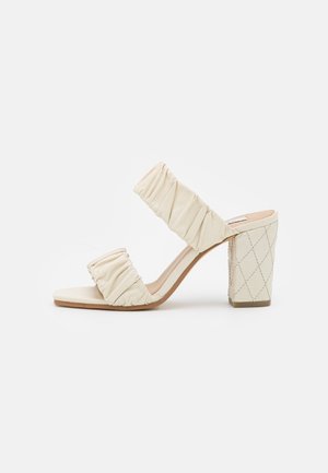 Beige sandal med åben tå og hæl, med to rynkede remme og quiltet blokhæl mod en hvid baggrund.