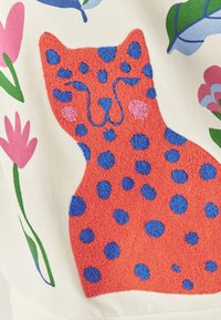 Ilustración de un gato texturizado en rojo y azul sobre un fondo crema, rodeado de flores rosas y hojas verdes. Tela suave con colores vibrantes.