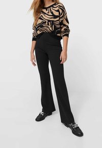 Czarne spodnie dzwony w połączeniu z beżowym swetrem z wyrazistym czarnym wzorem zebry. Sweter ma okrągły dekolt i luźny krój.