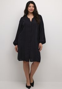 Vestido negro de botones con mangas largas, que presenta detalles de encaje en el frente, un corte relajado y una longitud hasta medio muslo. Textura de tejido suave.