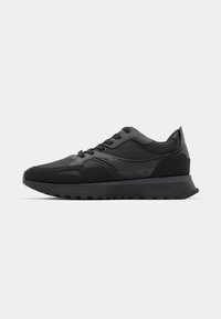 Svarte treningssneakers med en glatt overdel i lær og stoff, rund tå, snøring og en strukturert gummisåle. Diskret merkevare synlig.