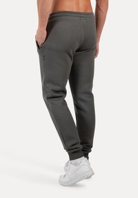 Pantalones de chándal grises con un diseño ajustado, cinturilla elástica, bolsillos laterales y puños de canalé, combinados con zapatillas blancas.