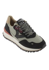 Sneaker a bassa altezza con pannelli neri, grigi e beige, lacci grigi e suola nera zigrinata, angolata per mostrare il lato esterno e la parte anteriore.