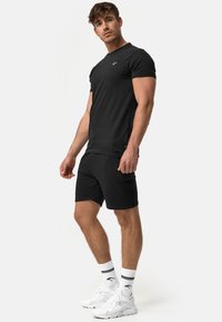 Camiseta negra de algodón y pantalones cortos a juego. La camiseta presenta un pequeño logo, combinada con zapatillas deportivas blancas y calcetines a rayas. Diseño simple.