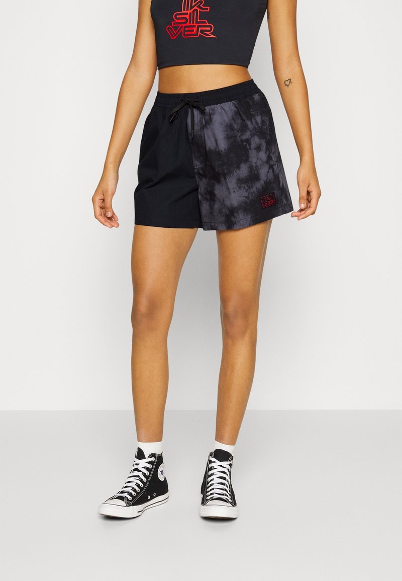 Černé a batikované šortky s elastickým pasem a šňůrkou; doplněné o krátký top a černé vysoké tenisky.