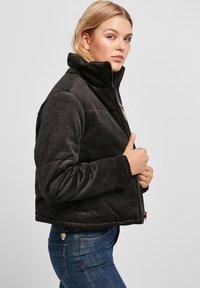 Zwarte corduroy jas met een hoge kraag, ritsluiting, geribbelde textuur en zijzakken, gedragen over blauwe denim spijkerbroek.