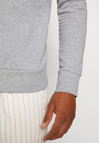 Šedá mikina s dlouhým rukávem s žebrovanými manžetami a lemem, doplněná světle barevnými pruhovanými kalhotami. Zaměření na texturu látky a střih.