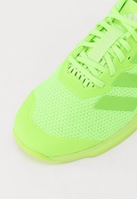 Neon green athletic shoe with a mesh upper, reinforced toe cap, and textured accents. Features polyester laces and branding details.