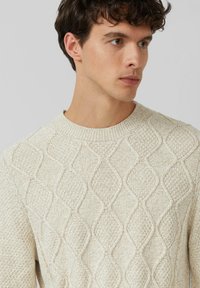 Beżowy sweter dzianinowy z wzorem w romby, okrągłym dekoltem i teksturowanym materiałem. Zbliżenie podkreśla szczegółowe przeszycia.