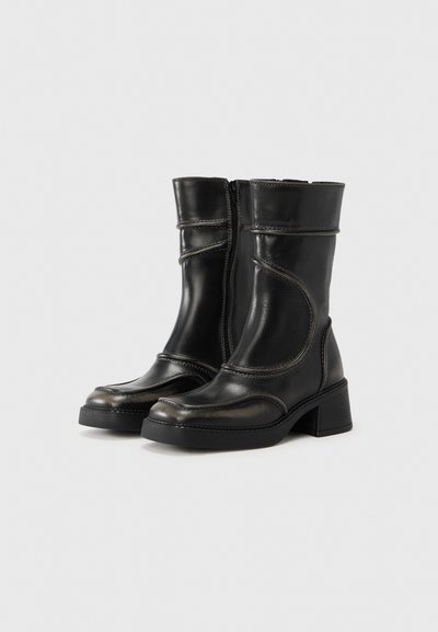 Μαύρα δερμάτινα μποτάκια αστραγάλου με χοντρό τακούνι, διαθέτουν φερμουάρ και λεπτομέρειες ραφής σε αντίθεση κατά μήκος του σχεδιασμού. Λείο υφή.