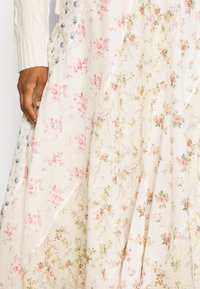 Blomstret stof, primært hvidt med pink og blå blomster, har en let tekstur. Designet inkluderer spredte blomster og bladagtige accenter.